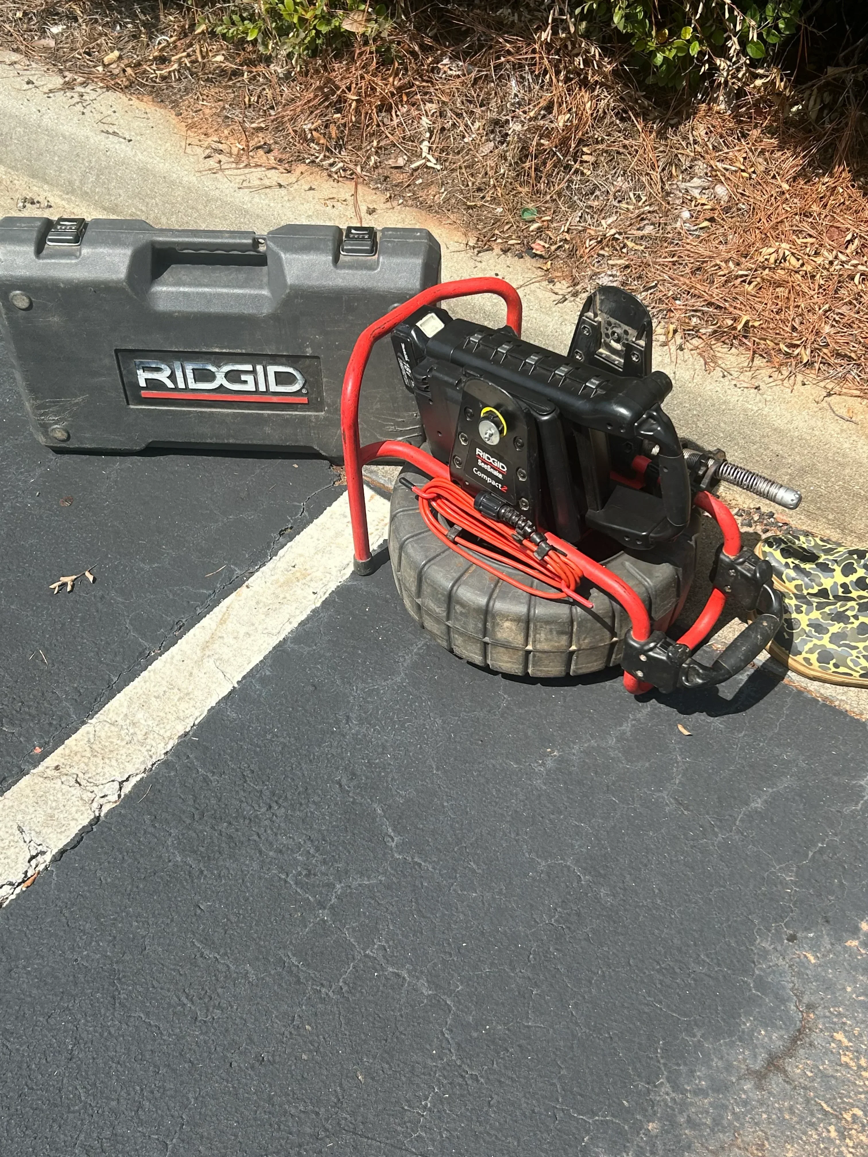 RIDGID drain camera inspection equipment with red cable and black carrying case on asphalt
