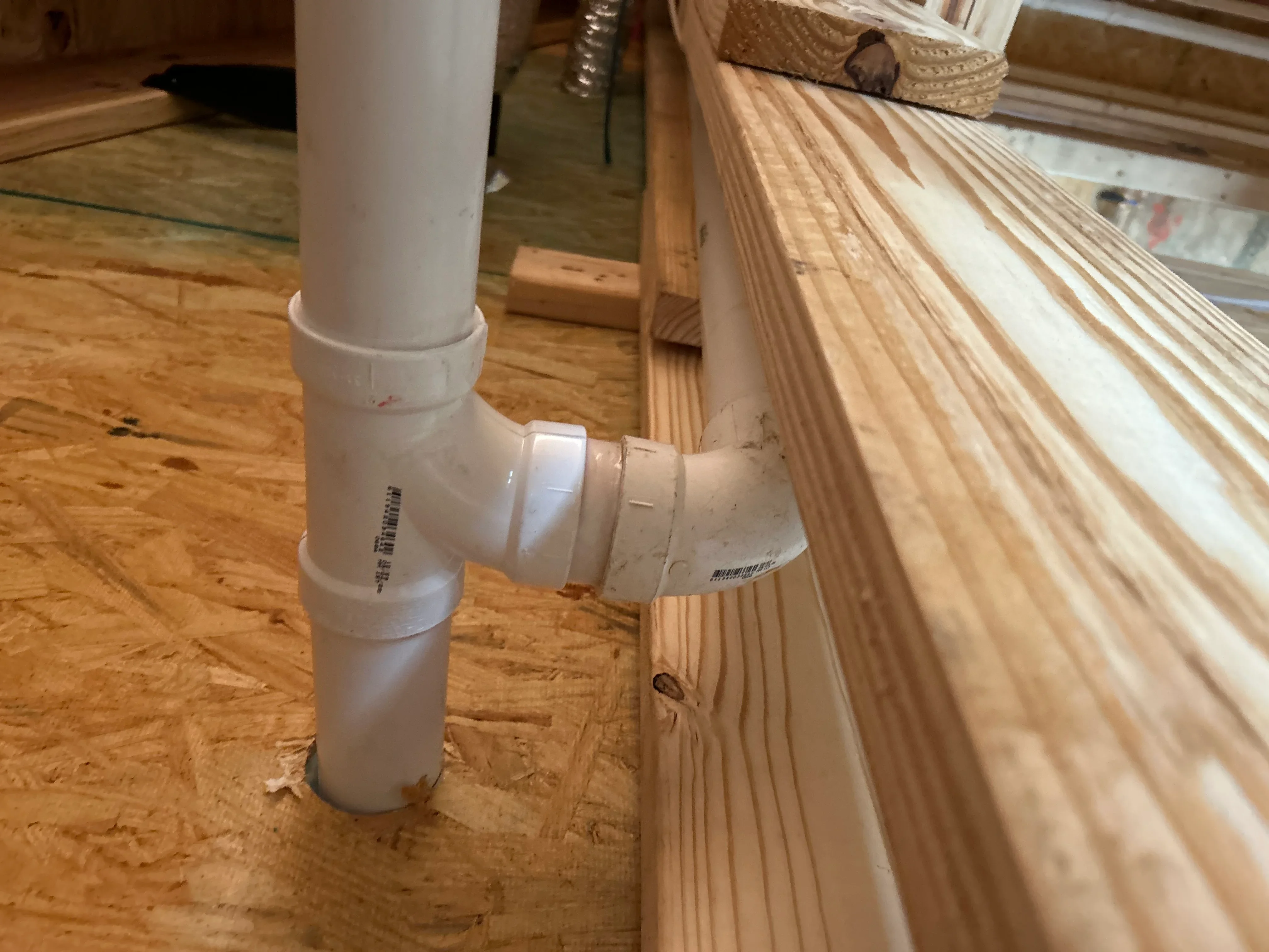 White PVC drain pipe with elbow fitting and cleanout installed against wooden framing