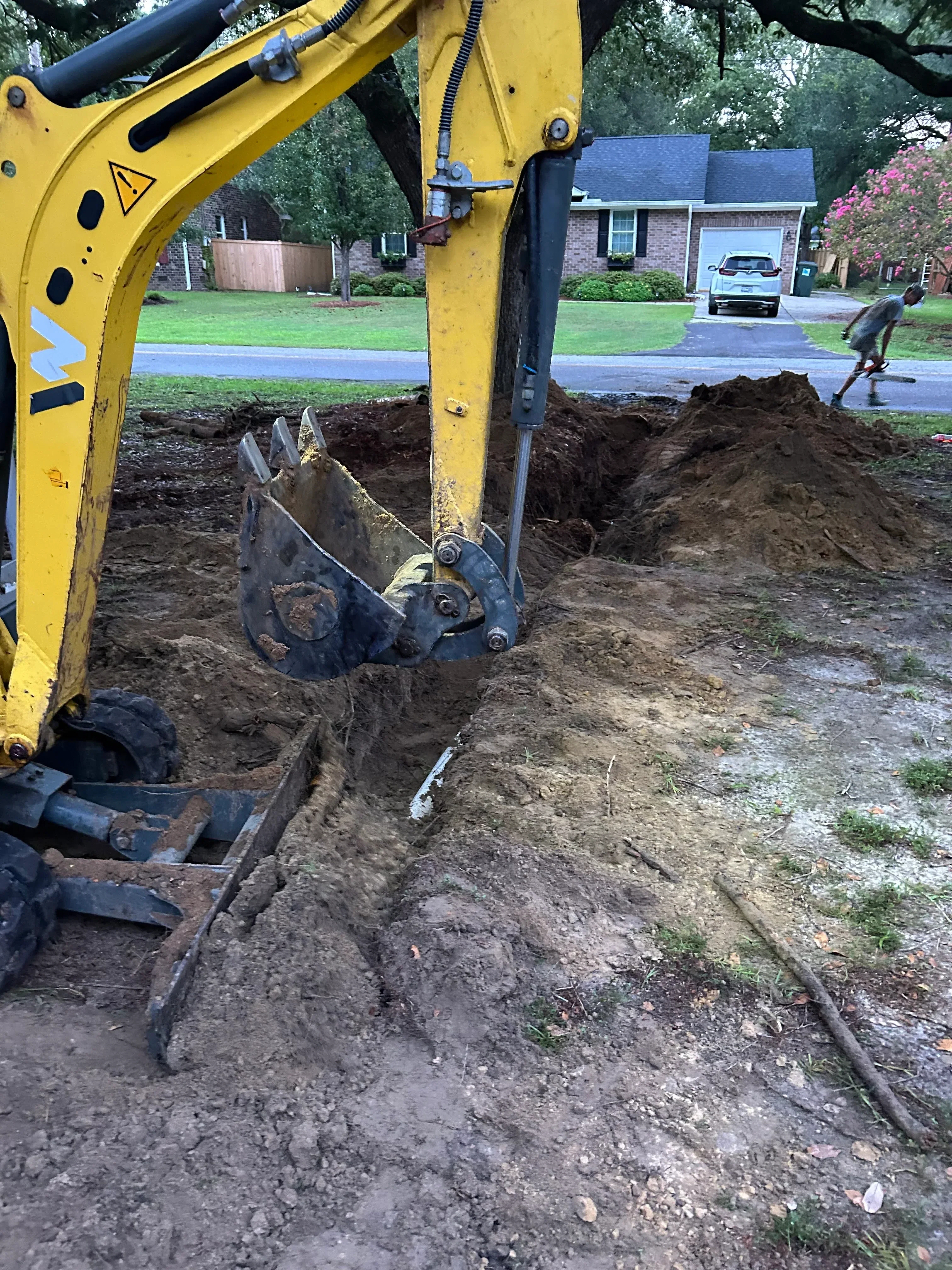 Mini excavator bucket exposing underground plumbing lines and soil during residential excavation