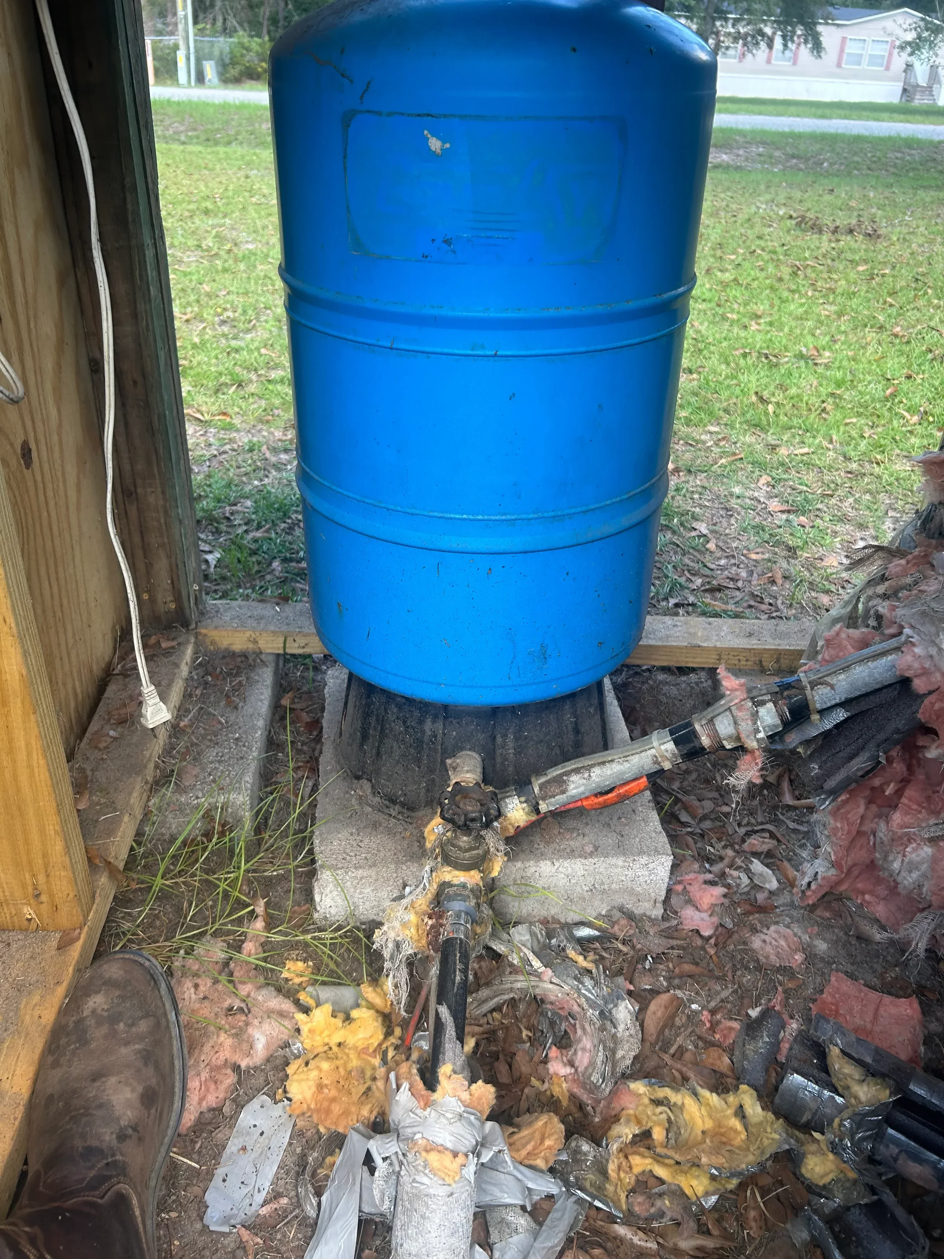 Blue plastic water storage tank with plumbing connections and valve assembly installed outdoors