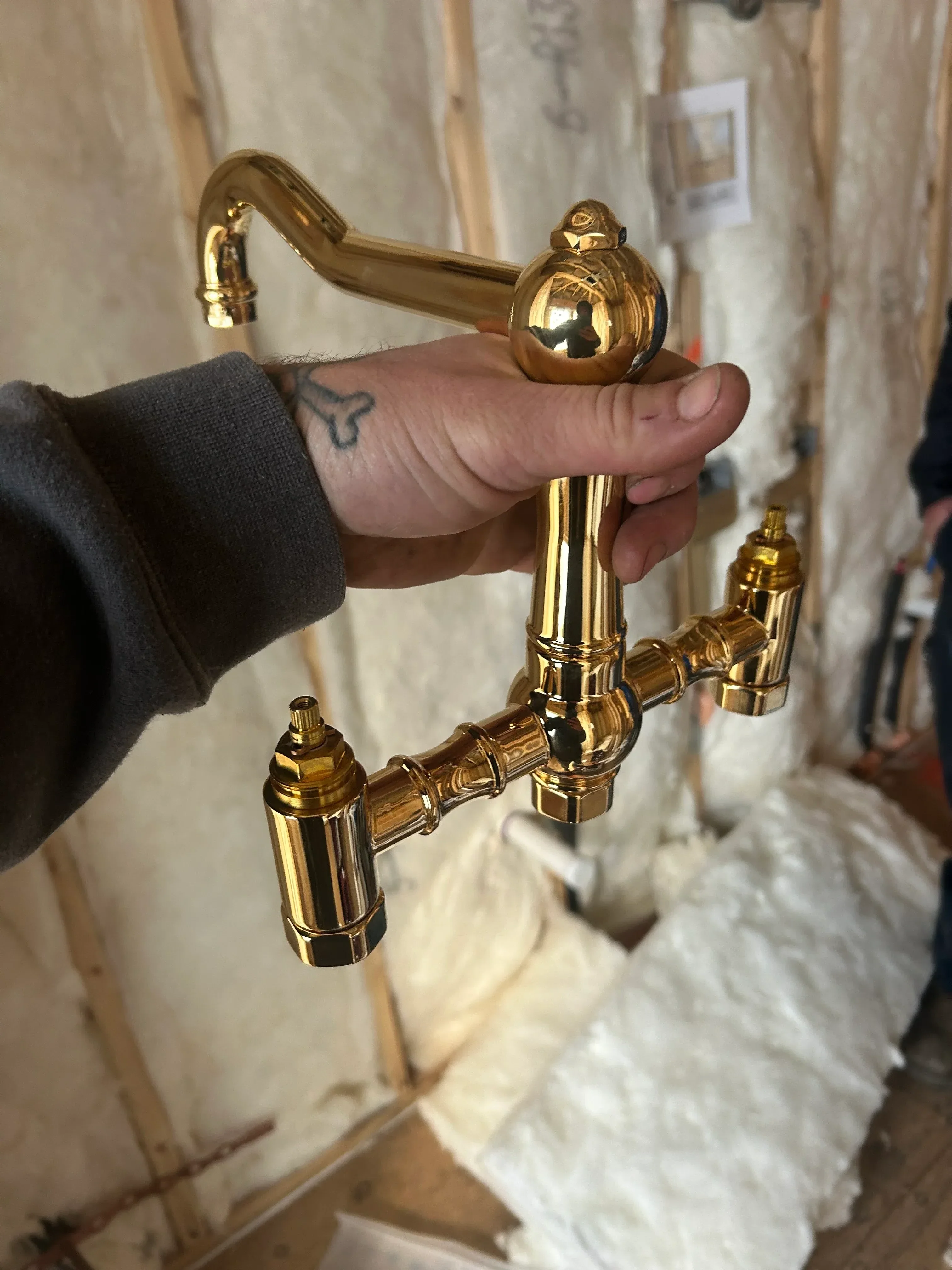 Polished brass dual-handle faucet with decorative spout and ball handles, held during installation