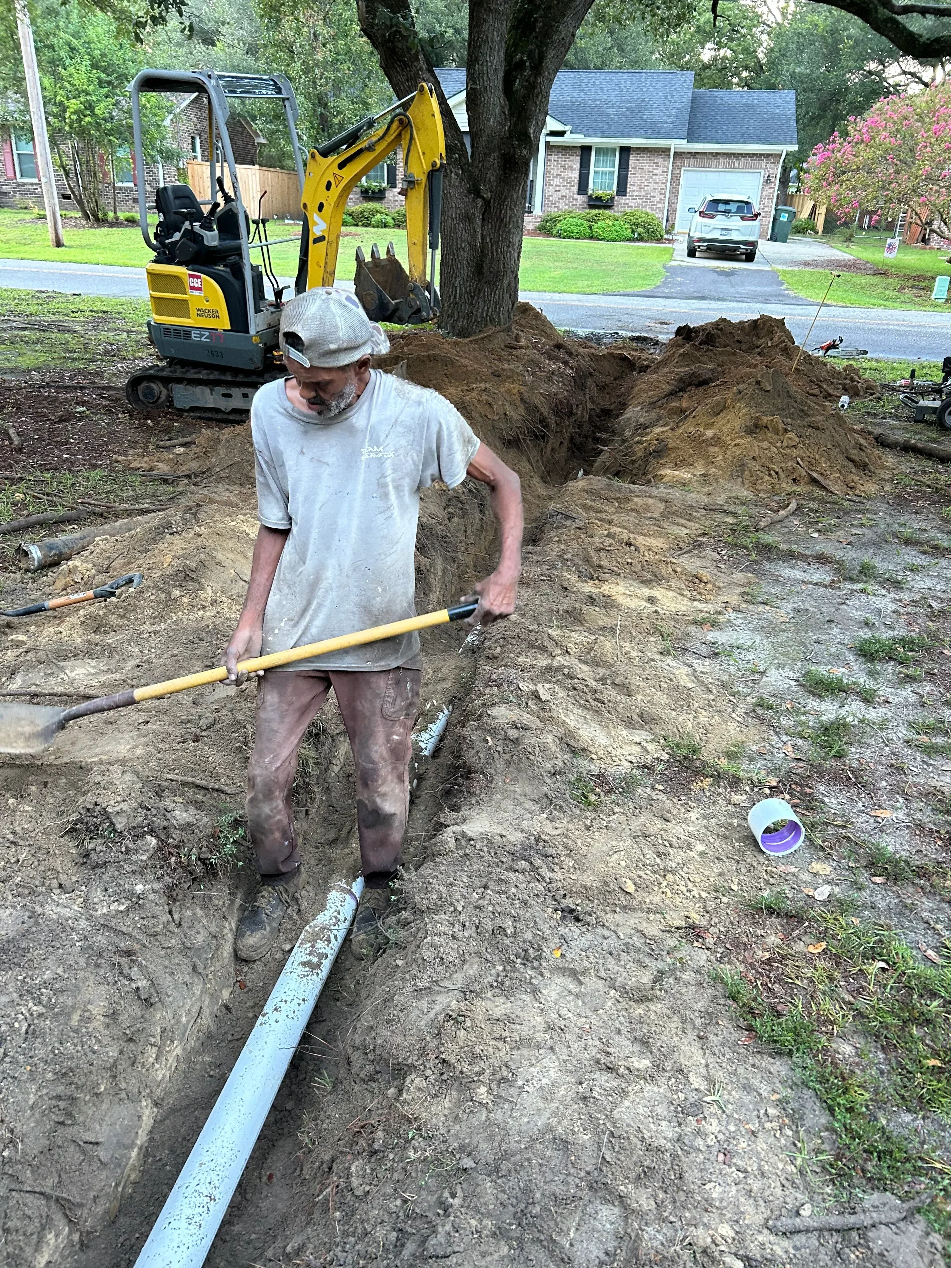 Worker with shovel excavating soil trench for underground plumbing installation