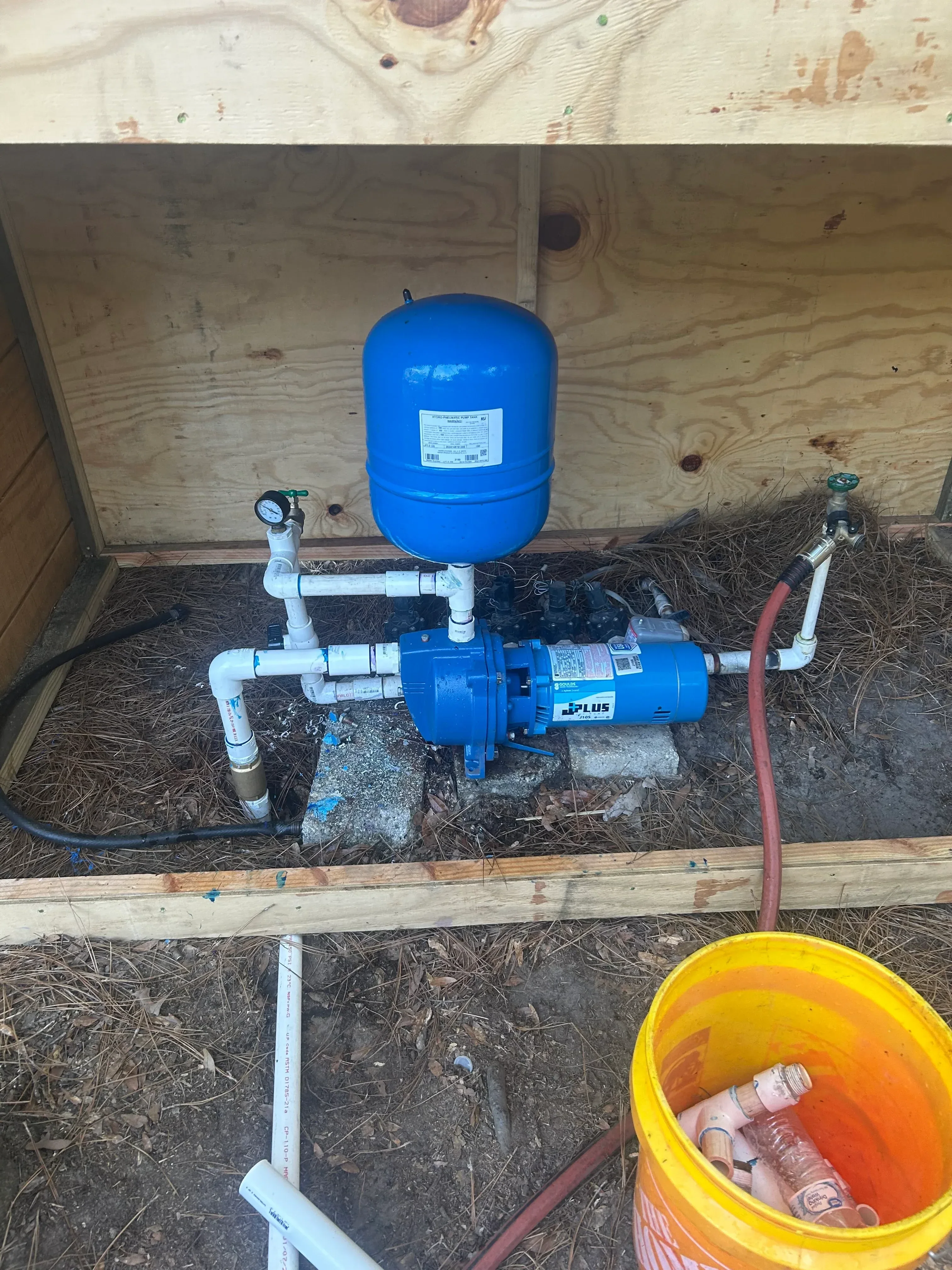 Blue pressure tank and submersible pump motor with PVC piping, pressure gauge, and check valve installation
