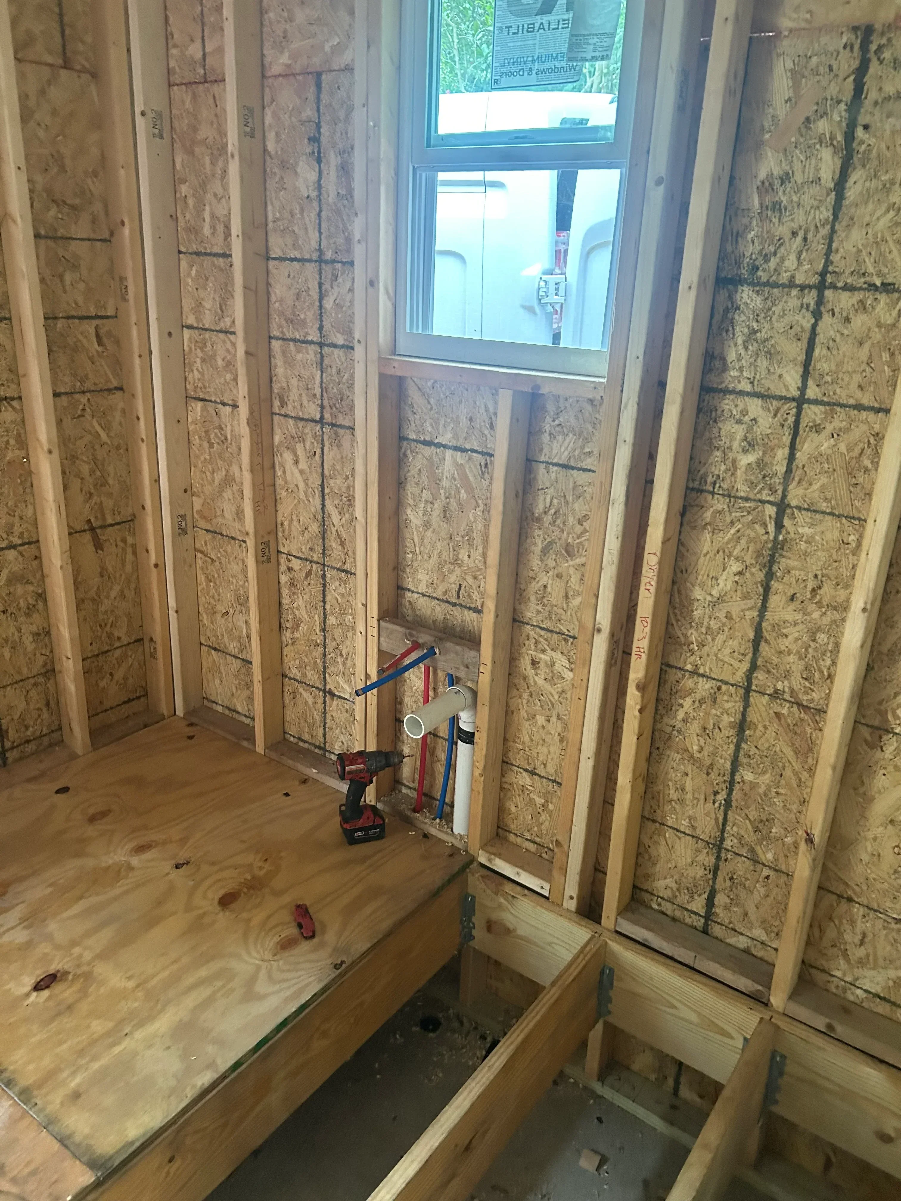 PEX supply lines and drainage pipes installed through wooden floor joists during rough-in phase