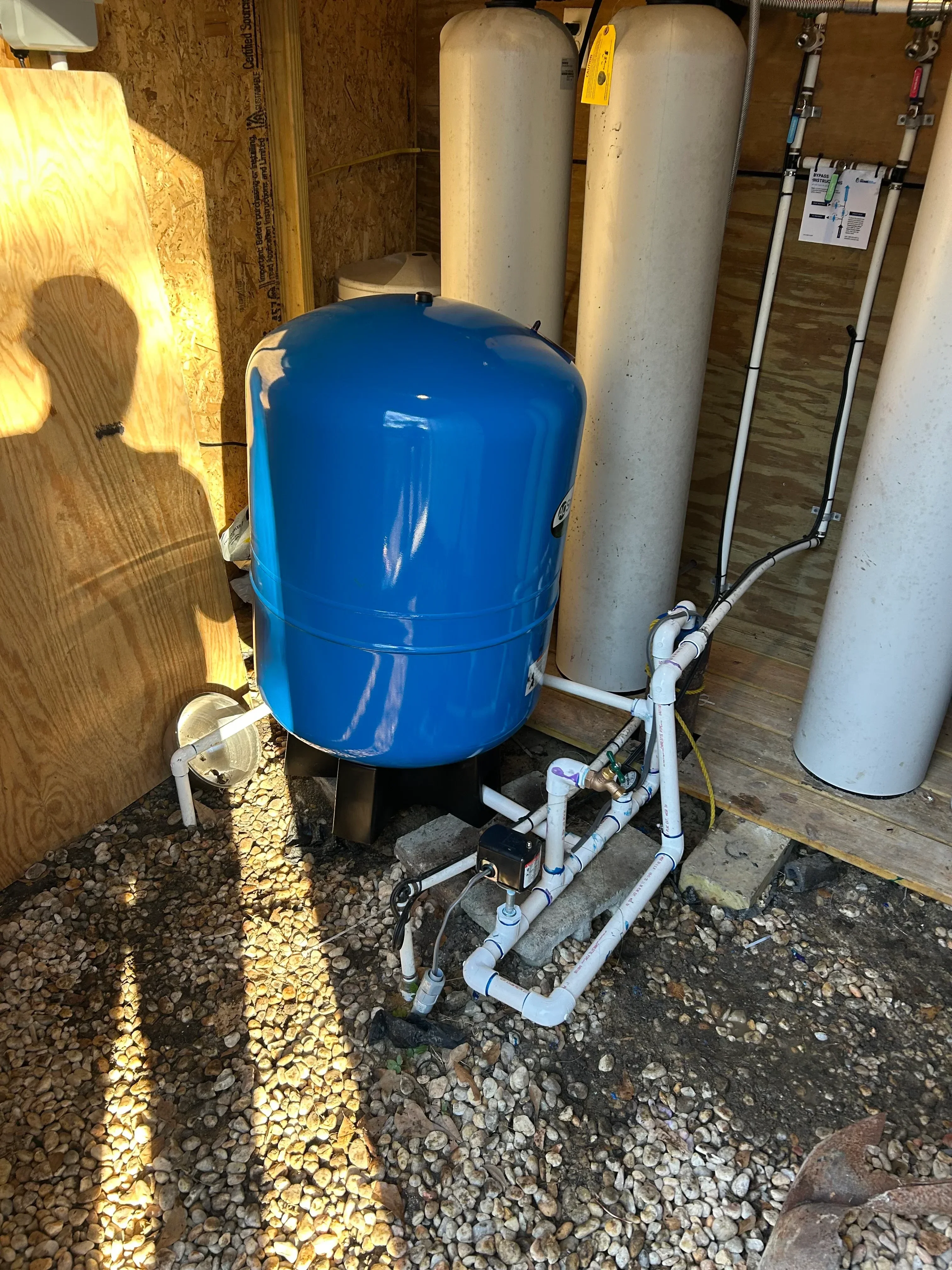 Blue pressure tank with pump, white PVC piping, and gray supply lines installed on wooden platform