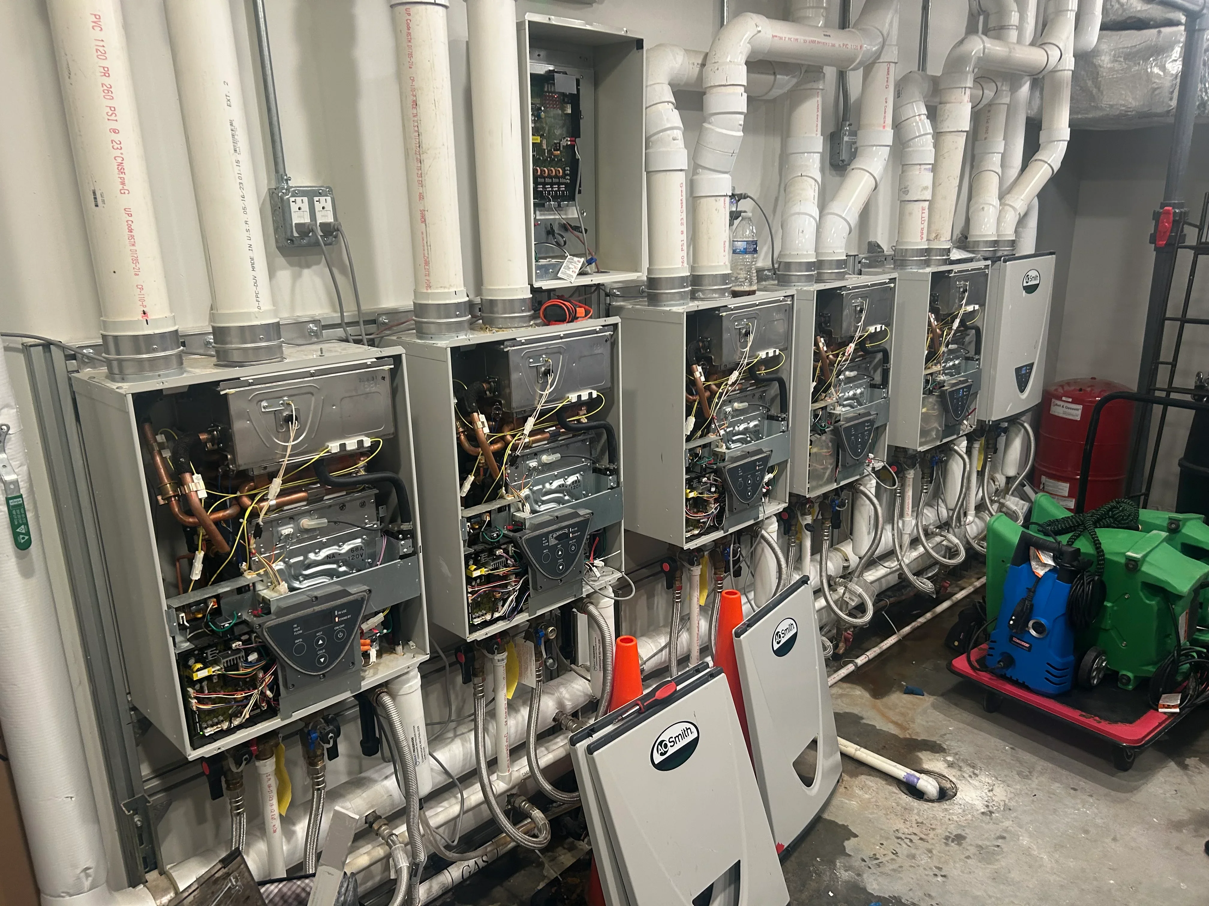 Five tankless water heaters with PVC venting, copper piping, and electrical connections installed in commercial space