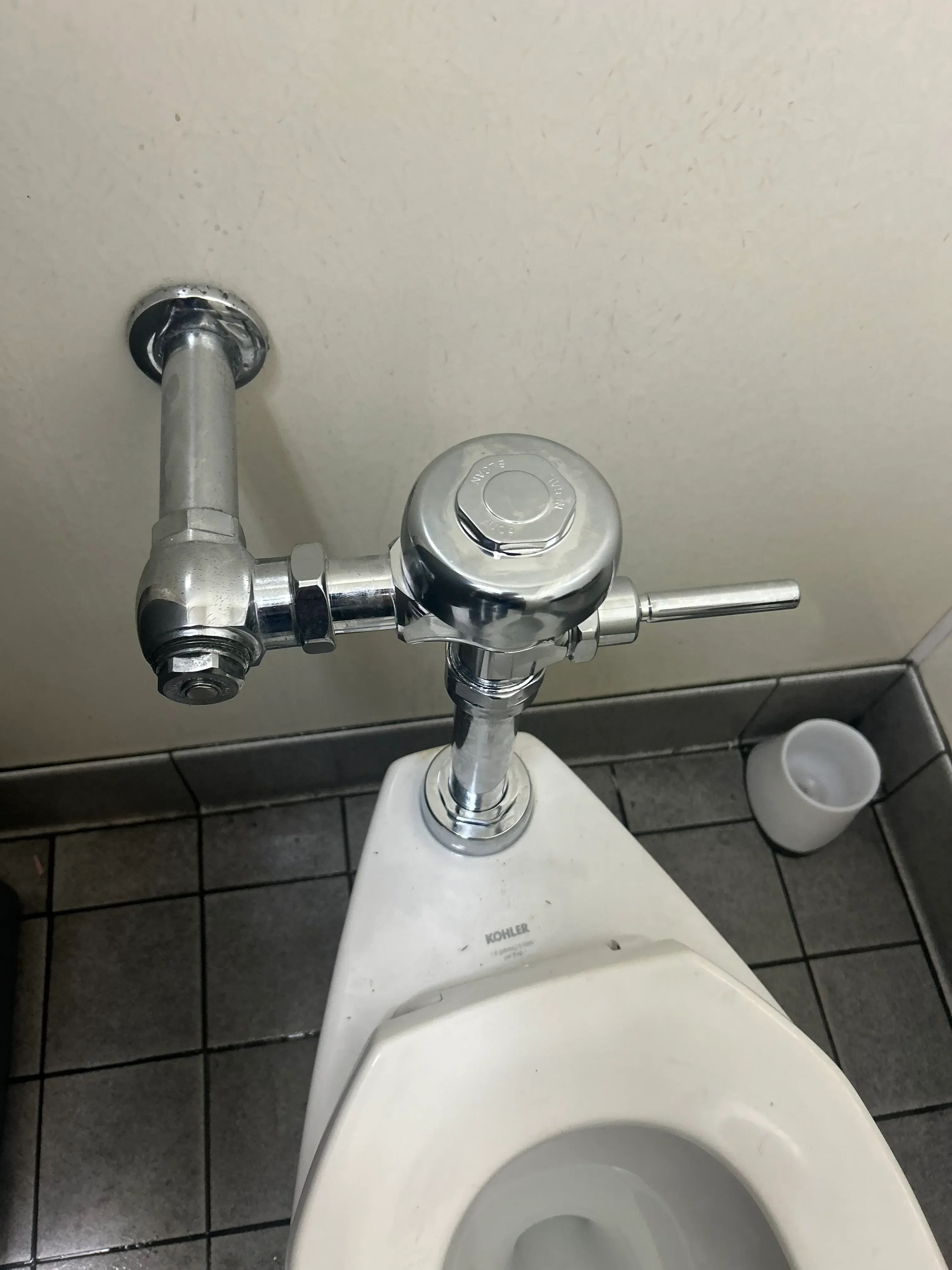 Chrome toilet supply line with shutoff valve installed on bathroom wall next to white toilet