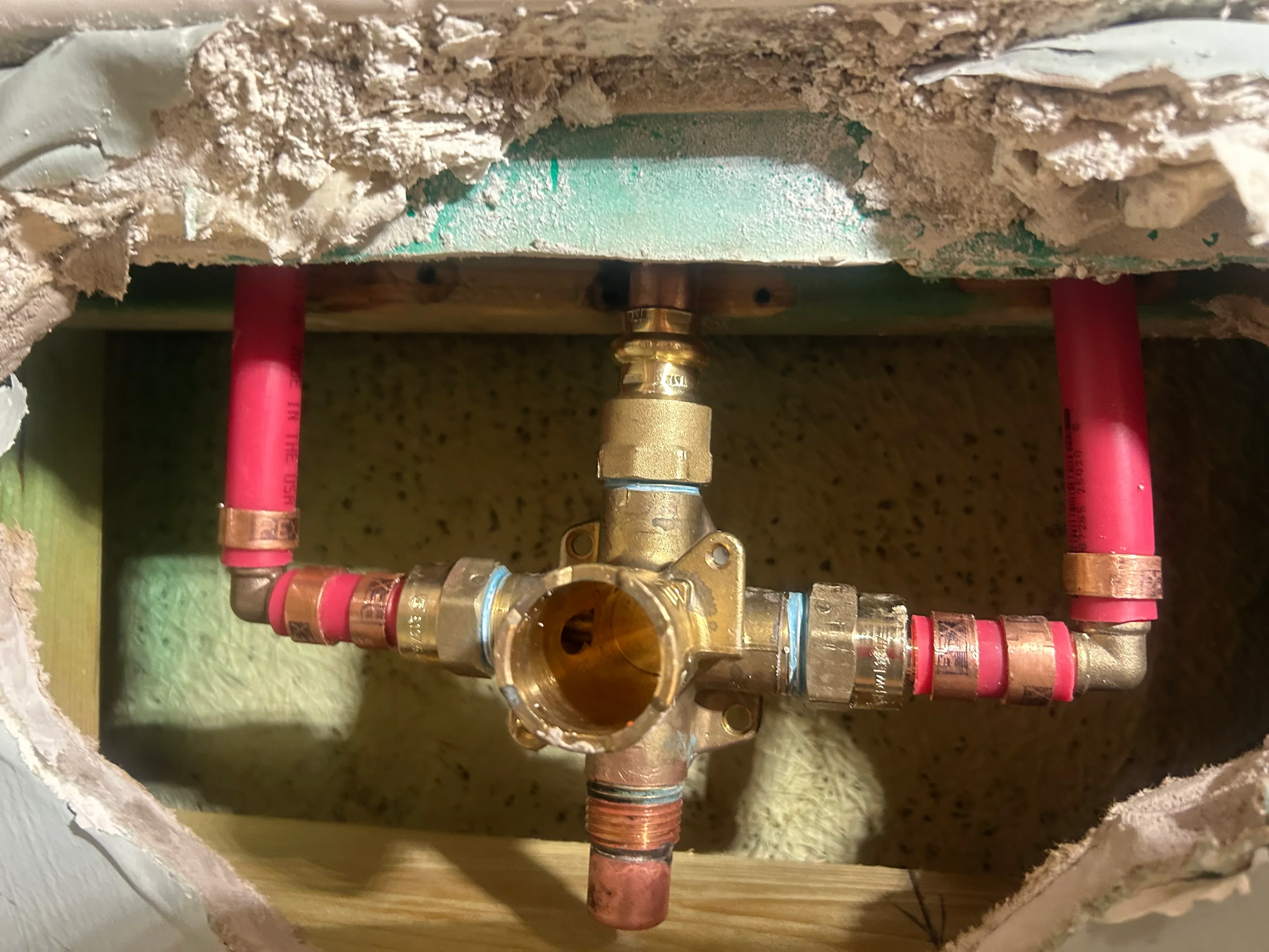 Brass ball valve with copper piping, red shut-off valves, and thread-seal tape in wall cavity