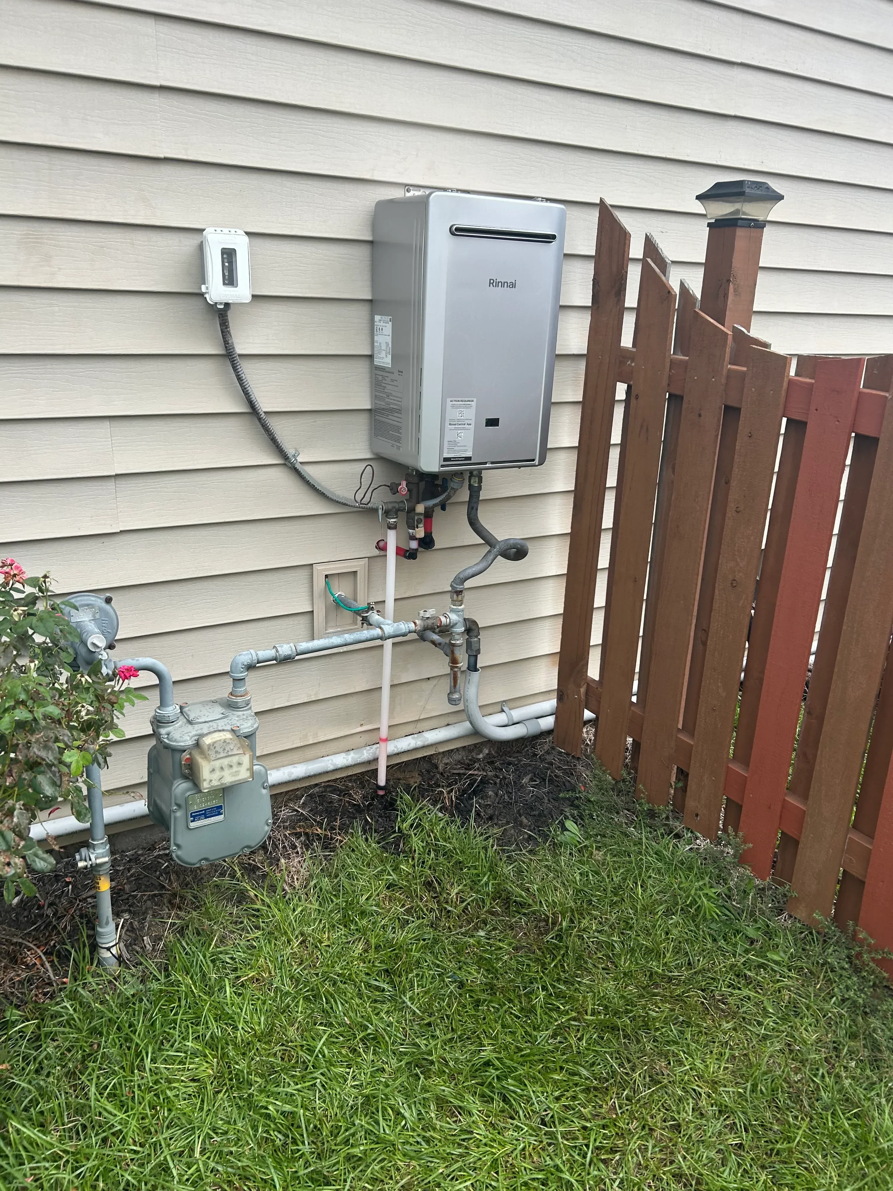 Tankless water heater with copper piping, valves, and gas connections on exterior wall