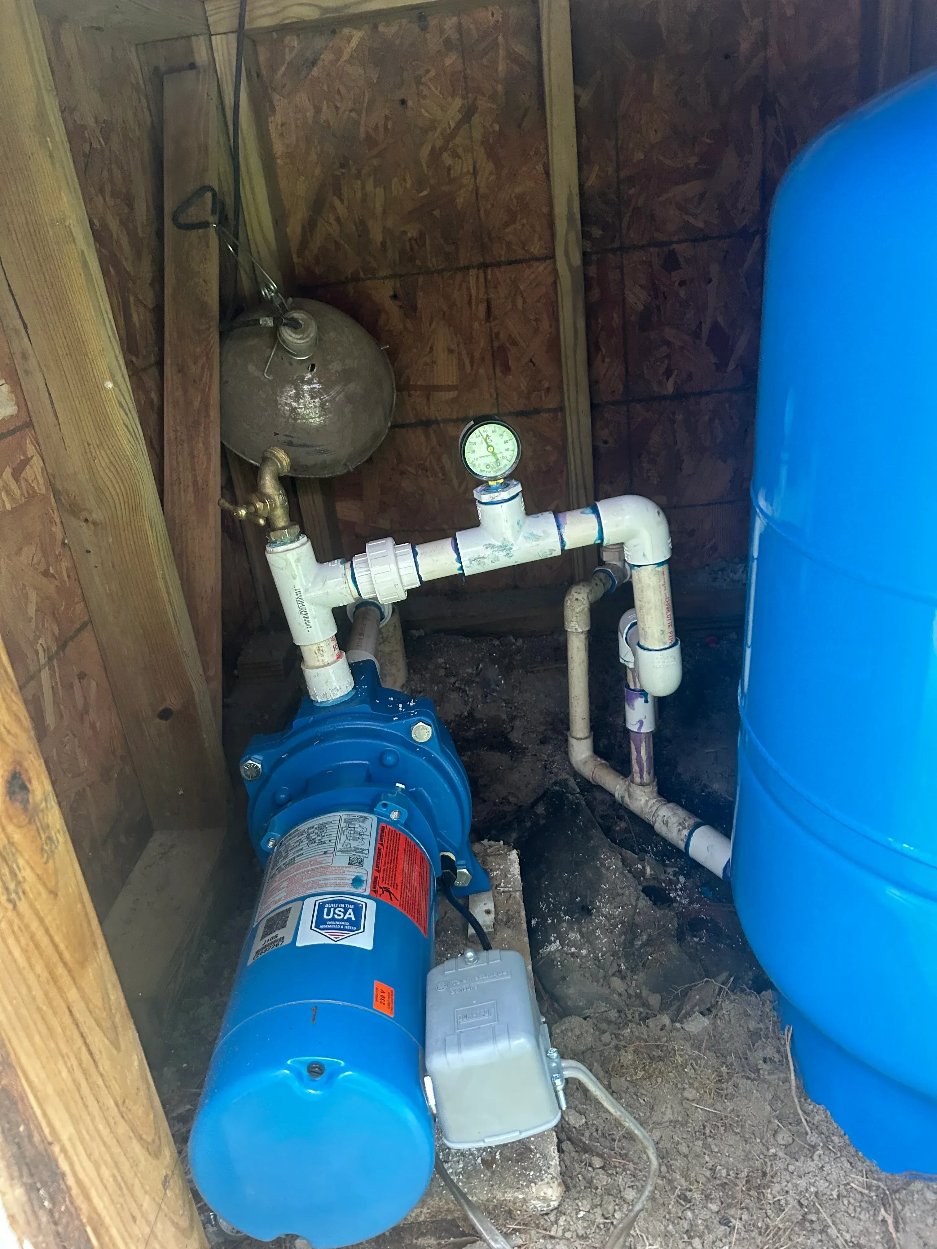 Well pump, blue pressure tank, and PVC piping with check valve and pressure gauge installed in pit