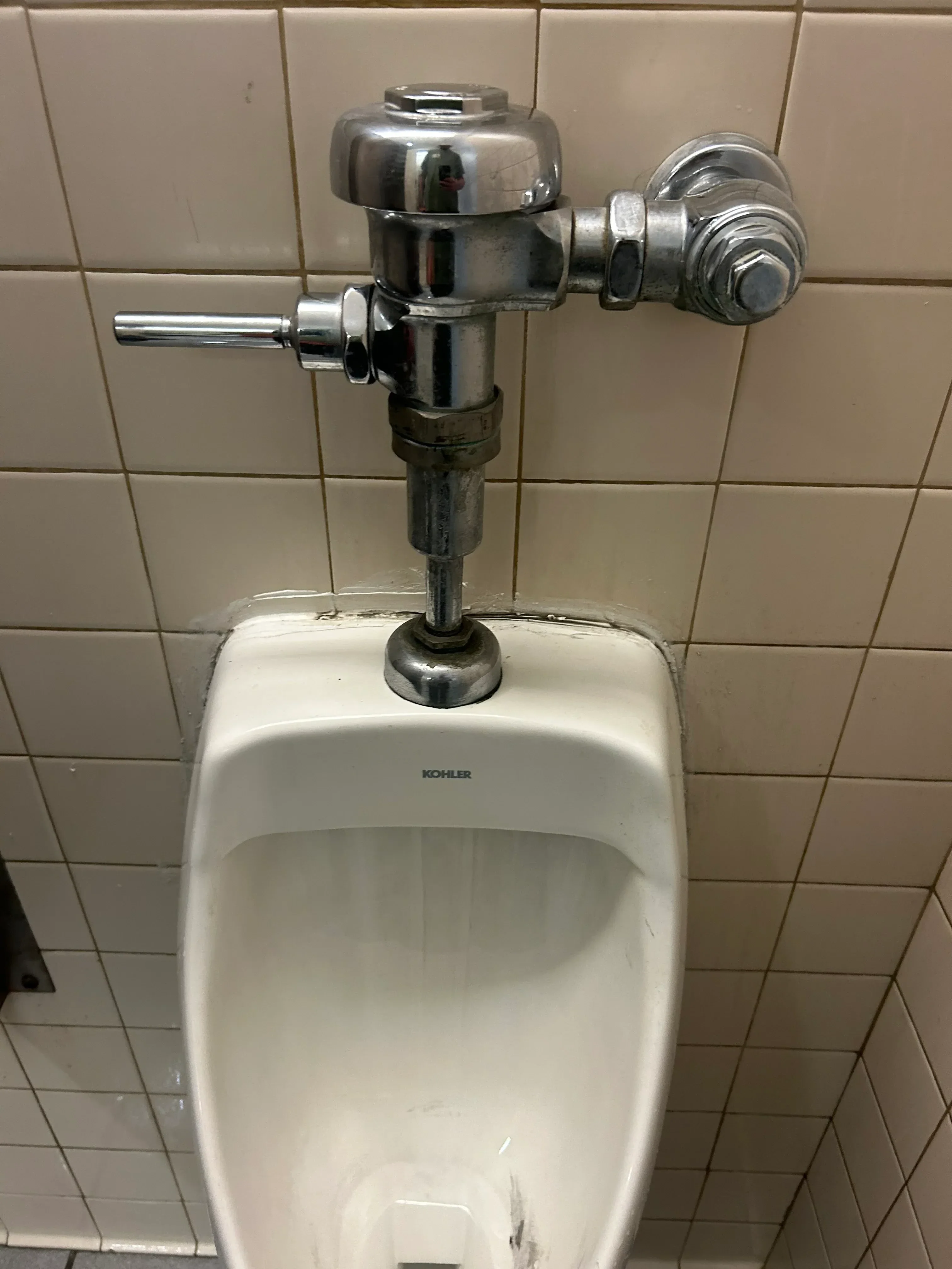 Chrome toilet fill valve and supply line installed on ceramic tile wall with white porcelain toilet