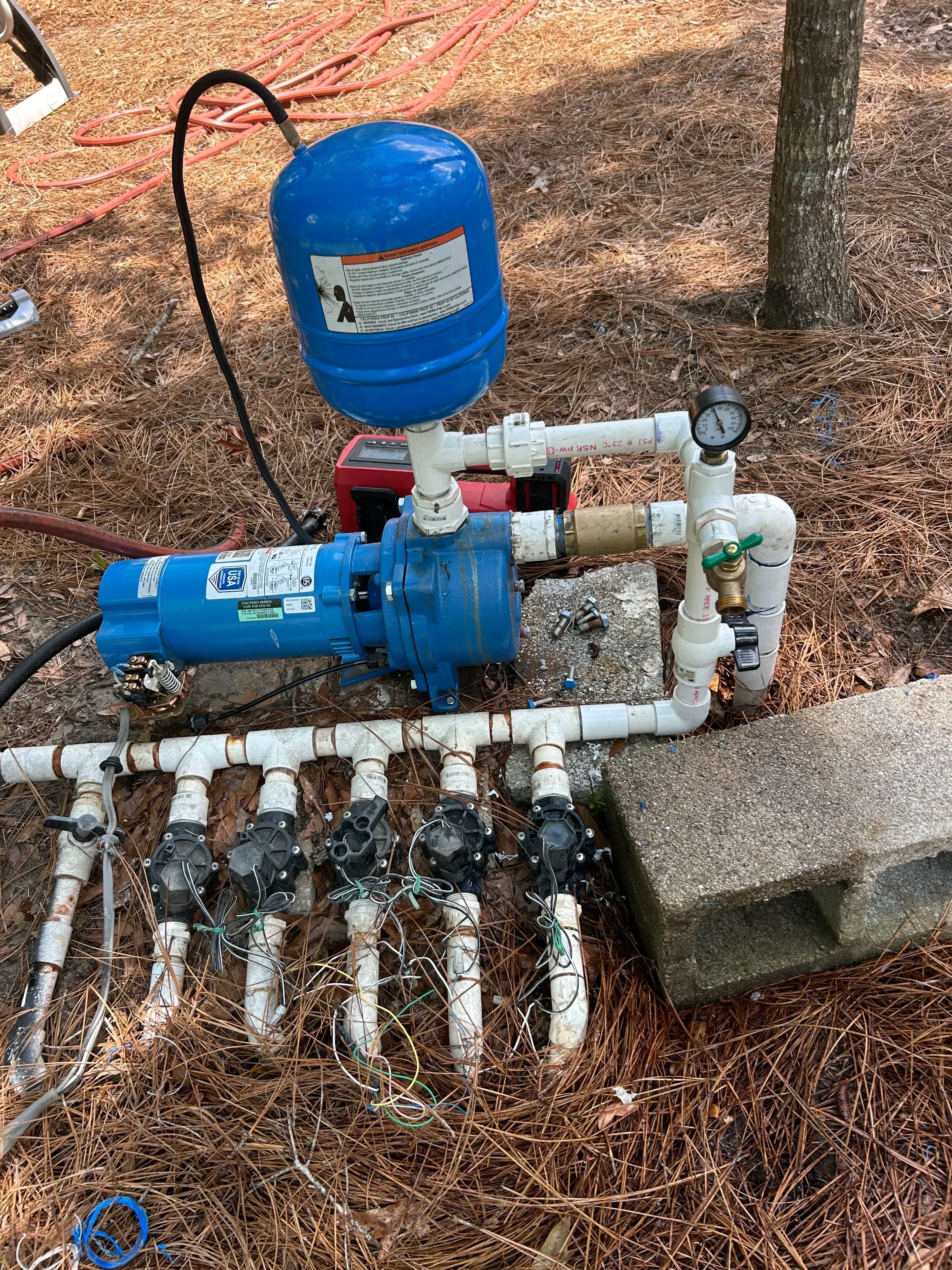 Blue pressure tank with pump assembly, PVC piping, pressure gauge, and solenoid valves for well water system