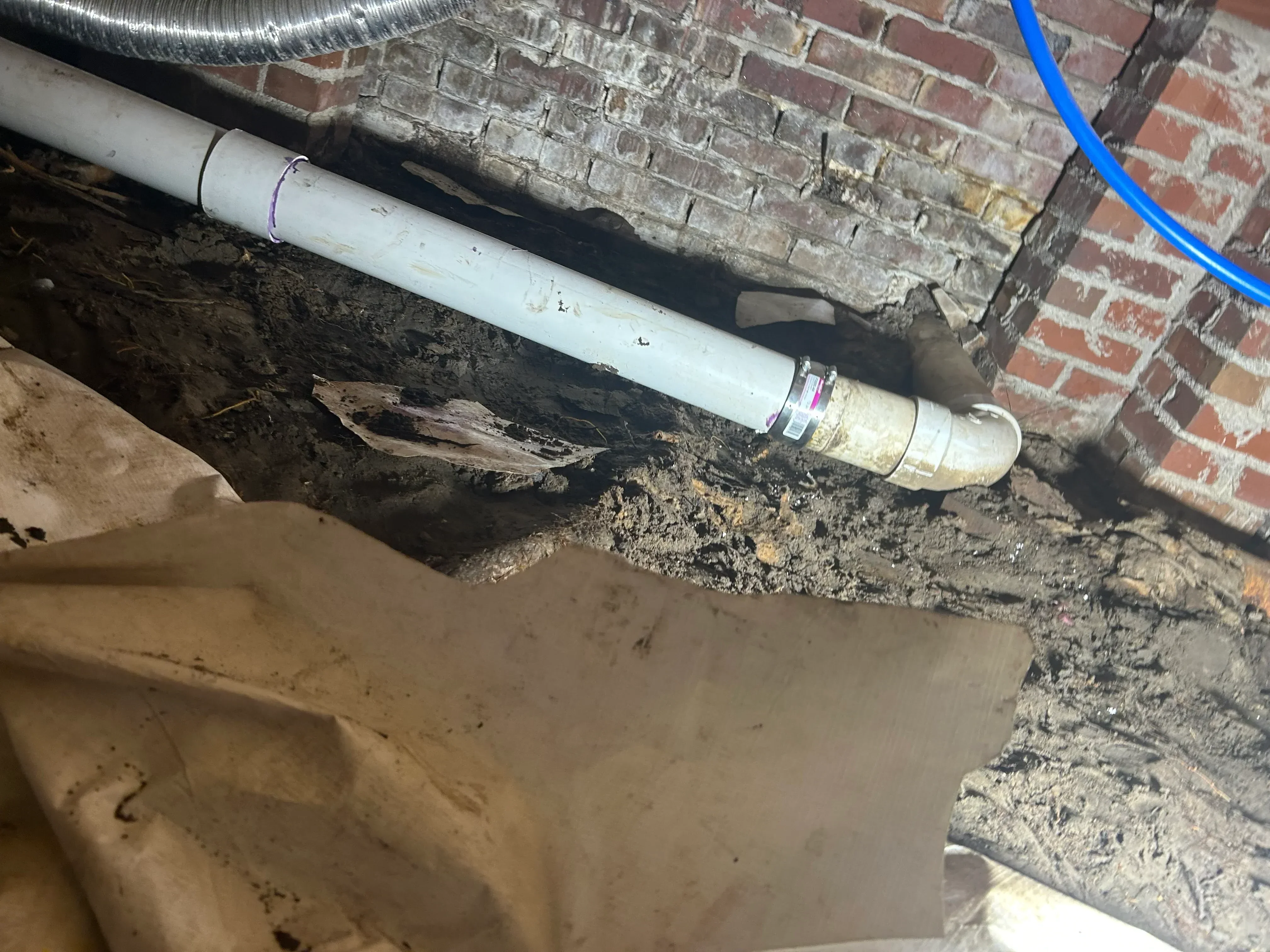 New white PVC drain pipe installed alongside deteriorated original line with brick foundation