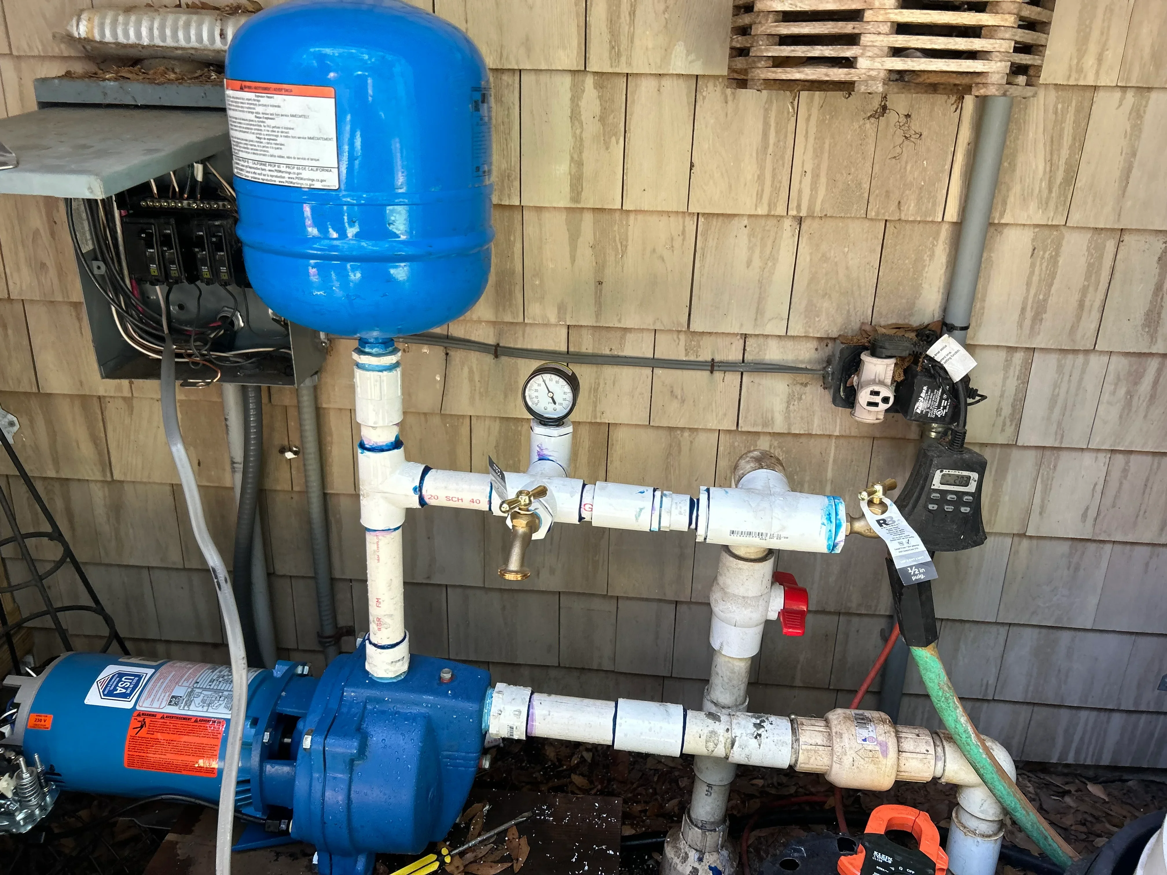 Blue well pump with pressure tank, gauges, brass valves, and sediment filters mounted on wooden wall